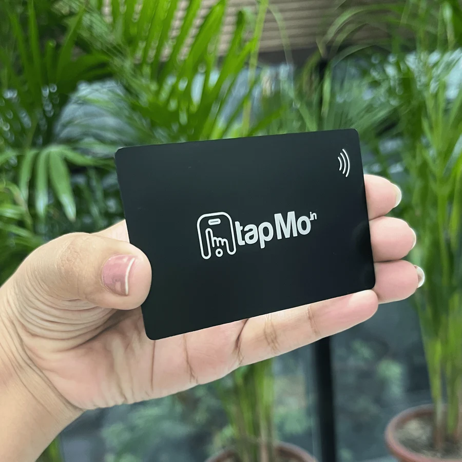 Black TapMo metal NFC card with silver engraving, held against green foliage